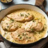 Baked chicken breast topped with creamy sauce and herbs in a casserole dish