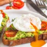 Avocado toast topped with a poached egg and cherry tomatoes on crispy bread.
