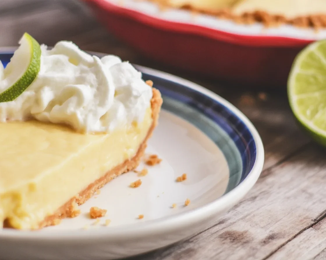 Slice of key lime pie with a homemade graham cracker crust on a white plate.