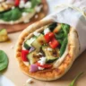 Pita bread breakfast wrap filled with hummus and scrambled eggs, garnished with fresh herbs.