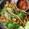 Vegan breakfast tacos with tofu scramble, avocado, and fresh veggies on a plate.